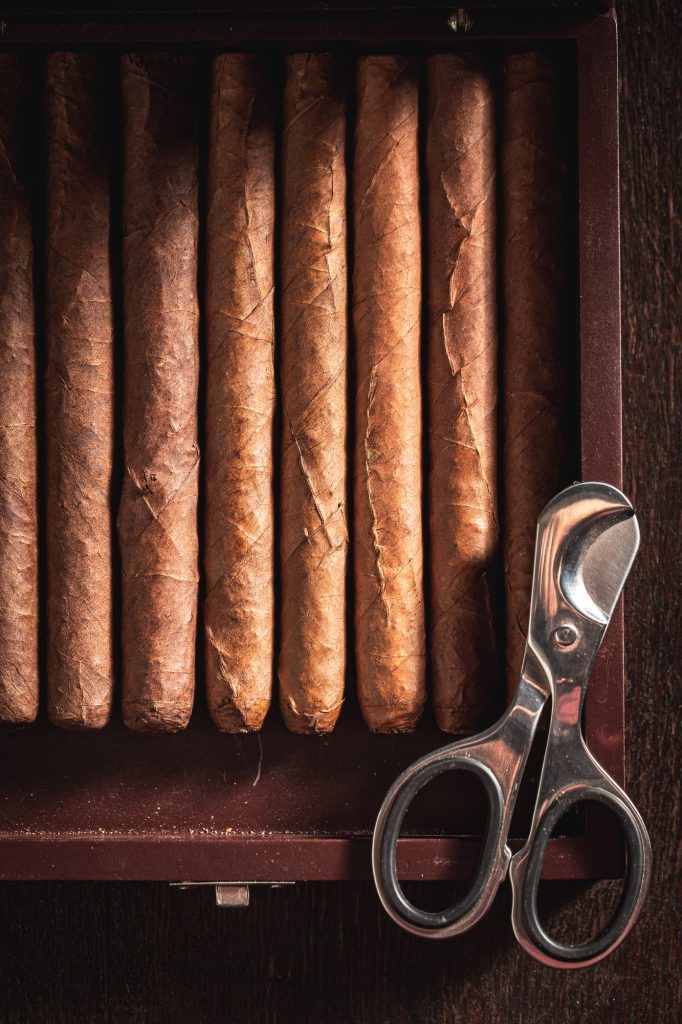 Metal scissors and cigars lay in wooden humidor